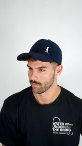 Gorra de béisbol confeccionada en pana color azul marino, con estructura de seis paneles y visera curva. Presenta un bordado pequeño en color blanco en el panel frontal.