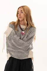 Buzo de tejido de punto con diseño geométrico en relieve, cuello redondo y mangas largas abullonadas con puños ajustables mediante lazos. Presenta un borde inferior en tejido acanalado de color crudo.