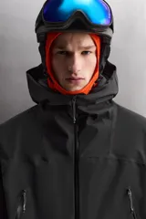 Cazadora deportiva de esquí en color negro, confeccionada en tejido técnico impermeable de tres capas con costuras y cremalleras termoselladas. Cuenta con capucha ajustable, ventilación en axilas, puños con ajuste de tira adherente y puño interior elástico con abertura para el pulgar. Incluye sistema de rescate RECCO y faldón interior para protección contra el frío.