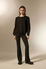 Blusa negra de poliéster con diseño texturizado de ondas, cuello redondo a la base y mangas largas transparentes con puños elásticos.