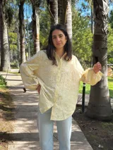 Camisa amarilla clara con bordado de flores blancas, de corte recto y mangas largas abullonadas.