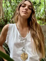 Collar largo con cadena plateada y dije circular dorado con textura irregular.