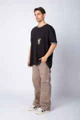 Remera negra de corte holgado con cuello y bordes de mangas en color verde oliva. Presenta un bolsillo frontal en el pecho con un estampado gráfico estilo sello postal que incluye la inscripción 'Horneros Argentina'.