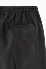 Pantalón de corte relajado y pierna recta, confeccionado en tejido suave de color negro. Presenta cintura elástica con cordón de ajuste, pliegues frontales y traseros, bolsillos laterales discretos y un bolsillo posterior insertado.
