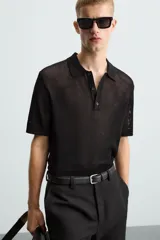 Polo de manga corta color negro, con cuello solapa y cierre frontal de botones. Confeccionado en tejido de punto con estructura abierta y calada.