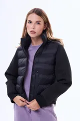 Campera negra de estilo híbrido, con cuerpo acolchado y mangas de tejido liso. Presenta cuello alto, cierre frontal y puños elásticos.