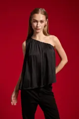 Blusa de poliéster color negro, con diseño asimétrico de un solo hombro, plisado ligero y corte holgado.
