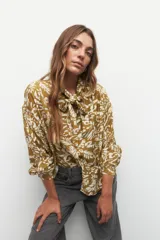 Camisa blanca con estampado floral en color marrón, de manga larga con puños abotonados, cuello con lazo y cierre frontal con botones.