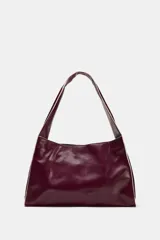 Bolso tipo shopper en formato horizontal, de efecto acharolado en color bordó con detalles de pespuntes en contraste. Cuenta con asa ancha de hombro, bolsillo interior con cierre y cierre principal con botón imantado.
