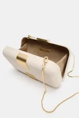 Bolso tipo clutch rígido de mano, color beige, con detalle de apliques metálicos dorados en el frente y cierre mediante clip. Incluye cadena extraíble para usar como bandolera.