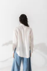 Camisa de lino color tostado, con cuello alto con volados, cierre frontal de botones y mangas largas con puños con volados.