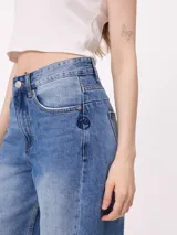 Jean de corte wide leg con diseño de pata ancha y costuras laterales decorativas. Presenta un lavado azul medio con efecto desgastado y ruedo desflecado.