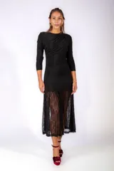 Vestido midi de color negro con acabado brillante, cuello redondo y mangas tres cuartos. Presenta un diseño ajustado en la parte superior con drapeado lateral y una falda inferior confeccionada en encaje transparente.