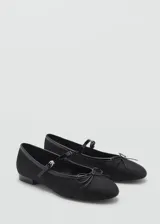 Zapato tipo bailarina color negro, con punta redonda, tira sobre el empeine con hebilla y moño decorativo.