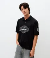 Polo de manga corta con cuello camisero y cierre frontal de botones. Presenta un diseño boxy fit con estampado gráfico en el pecho y detalle en la manga. Confeccionada en tejido técnico de microfibra.
