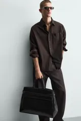 Bolso de mano extragrande negro de cuero sintético, con compartimento principal con cierre de imán, bolsillo interior con cierre y bolsillo secundario con solapa y detalle de cinta. Cuenta con dos asas de mano.