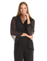 Enterito negro de seda fría con escote en V cruzado, mangas largas voluminosas de gasa transparente con puños elásticos fruncidos. Tiene cintura elástica interna, lazo lateral ajustable y pierna de corte recto al tobillo.