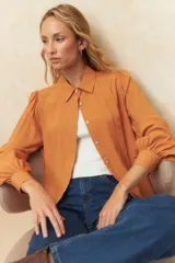 Camisa color naranja con cuello clásico, abotonada al frente, mangas largas abullonadas y corte relajado.