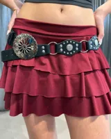 Cinturón negro de cuero sintético con diseño western, compuesto por una hebilla circular grande con grabado floral y piezas decorativas con tachas metálicas unidas por argollas plateadas.