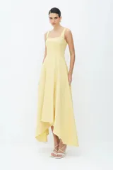 Vestido midi de algodón compacto, de color blanco, con corte entallado en el torso y falda amplia de corte asimétrico, más corta adelante y larga atrás. Presenta escote cuadrado y tirantes anchos.