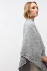 Ruana de tejido de punto grueso en color gris, con diseño de cuello alto y terminaciones acanaladas en los bordes.