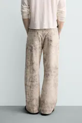 Pantalón de corte baggy fit confeccionado en tejido de algodón con efecto lavado y estampado abstracto en tonos beige y gris. Presenta diseño de cinco bolsillos, cierre frontal con cremallera y botón.