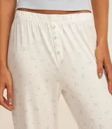Conjunto de pijama largo de rib más sostenible, compuesto por una blusa de manga corta con escote redondo y detalle de flor aplicada, y un pantalón largo con cintura elástica, detalle de botones y estampa floral total.