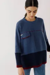Buzo de tejido de punto en color azul, con diseño de bloques de color en azul marino y detalles en bordó. Presenta un bolsillo frontal con costuras decorativas a contraste y puños acanalados.