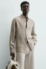 Camisa de manga larga color beige claro, confeccionada en lino, con cuello italiano y cierre frontal de botonadura.