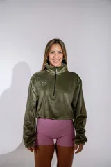Buzo de plush color verde oliva, con cuello alto y cierre frontal parcial. Presenta mangas largas con puños elásticos y un pequeño bordado en el pecho.