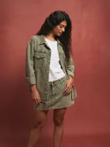 Sobrecamisa verde grisáceo de denim con cuello camisero, cierre frontal con botones, bolsillos con solapa en el pecho y mangas largas con puños abotonados.