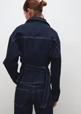 Chaqueta estilo tejano vaquero de algodón con elasticidad, color azul marino. Cuenta con cuello camisero, cierre frontal con botones, dos bolsillos de parche con solapa y botón en el pecho, mangas largas con puños abotonados y tira ajustable en la parte posterior.