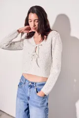 Cardigan de punto color beige claro con motas oscuras (tweed), manga larga y escote en V. Se cierra mediante lazos cruzados en el frente.