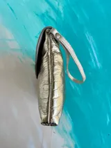 Sobre de mano Carolina De Cunto modelo Saria, confeccionado en cuero dorado brillante con textura y solapa plateada con detalles pintados a mano. Cuenta con tira de muñeca y cierre con broche imán.