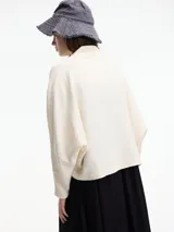 Cardigan de tejido de punto color beige, con cuello chal, manga amplia y bolsillos laterales.