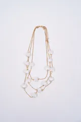 Collar multicapa de cadena dorada fina con dijes colgantes en forma de conchas marinas blancas.