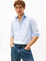 Camisa de popelín de algodón celeste con sutiles rayas verticales blancas, de corte regular, manga larga y cuello camisero con botones. Presenta cierre frontal con botones y el logo bordado de Tommy Hilfiger en el pecho.
