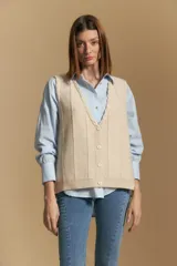 Chaleco tejido de punto color beige, con escote en V, cierre frontal con botones y diseño de líneas verticales. Presenta terminaciones acanaladas en el ruedo y un delicado borde trenzado en el escote.