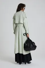 Trench color verde claro con cuello solapa, doble botonadura, cinturón y bolsillos laterales.
