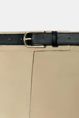 Bermuda larga de tiro medio color beige, con bolsillos en el delantero, pinzas y cierre frontal con cremallera y ganchos metálicos. Incluye cinturón fino de cuero sintético negro con hebilla metálica.
