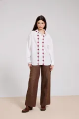 Camisa blanca de corte holgado con cuello camisero y cierre frontal de botones. Presenta un delicado bordado vertical de flores pequeñas en color bordó a lo largo de la botonera y en el cuello.