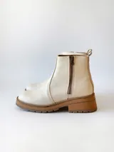 Bota corta de cuero vacuno con textura granulada, color crudo. Presenta cierre lateral metálico, suela track de goma en tono suela y tirador trasero.