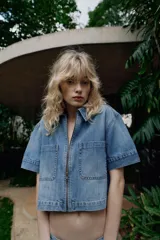 Camisa de denim de corte recto y manga corta, con cuello solapa, cierre frontal con cremallera y dos bolsillos delanteros de plastrón.