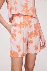 Bermuda de tela estampada con flores color naranja sobre fondo rosa pálido, con cintura elastizada y bolsillos laterales.