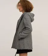 Saco largo con capucha y estampado pied de poule en blanco y negro. Tiene cuello alto, cierre con botones y cremallera, bolsillos y mangas largas.