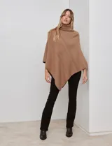 Poncho tejido color crema, con cuello polera y diseño trenzado diagonal en el frente. Presenta un corte asimétrico en el ruedo.