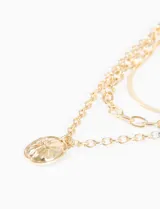 Collar de tres cadenas doradas superpuestas con dijes colgantes: una cadena de eslabones gruesos, una cadena de eslabones más finos y una cadena tipo serpiente. Incluye un dije ovalado con relieve de un racimo o sol.