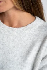Sweater de punto gris melange, de manga larga y cuello redondo. Presenta un detalle de botones marrones en el lateral.
