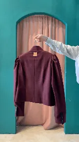 Chaqueta corta verde oscuro de paño, con cuello mao, hombros fruncidos con mangas abullonadas y cierre frontal de botones dorados. Presenta detalles de bordados dorados en el frente y puños con tajo.