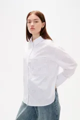 Camisa de algodón blanca con estampado de corazones formados por pequeños cristales de strass. Presenta cuello clásico, cierre frontal con botones, bolsillo en el pecho y mangas largas con puños abotonados.